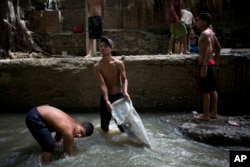 In this Nov. 30, 2017 photo, Douglas, center, holds a sack in the polluted Guaire River as he and others pull mud up from the bed of the river in search of gold and other valuables to sell, in Caracas, Venezuela.