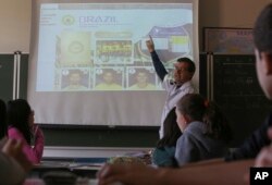 FILE - Ari Mascarenhas teaches students Portuguese using the World Cup sticker book, in Sao Paulo, Brazil, May 21, 2018.