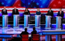 Democratic presidential candidates raise their hands when asked if they would provide healthcare for undocumented immigrants, during the Democratic primary debate, June 27, 2019, in Miami.