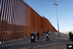 Border Patrol agents and others stand next to a new stretch of border wall in Calexico, Calif., Oct. 26, 2018.