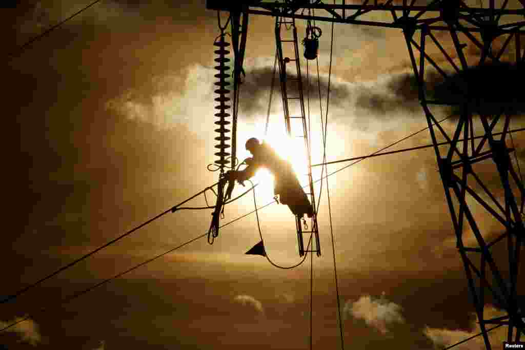 A technician works on an electricity tower as part of repair of high-tension electricity power lines, during sunset in Roye, France.