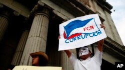 A masked man holds up a sign that reads "FCN Corruption," referring to the ruling party, Frente Convergencia Nacional, as he and others protest Guatemala's President Jimmy Morales at Constitution square in Guatemala City, April 21, 2018. 