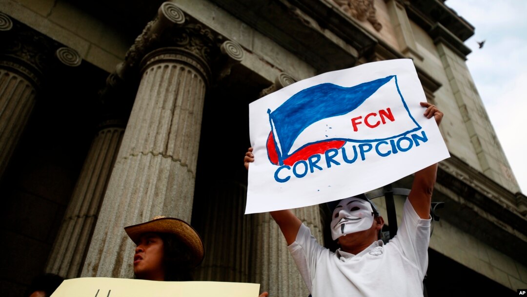 A masked man holds up a sign that reads "FCN Corruption," referring to the ruling party, Frente Convergencia Nacional, as he and others protest Guatemala's President Jimmy Morales at Constitution square in Guatemala City, April 21, 2018. 