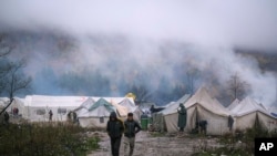 In this Wednesday, Nov. 20, 2019, photograph, migrants walk at the Vucjak refugee camp outside Bihac, northwestern Bosnia. Hundreds of refugees and migrants remain stuck in northwest Bosnia in a makeshift camp described by numerous international organizations as dangerous.