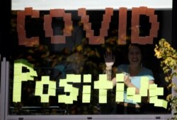 People wave through the window of a student accommodation building with a 'Covid Positive' sign displayed in it, following the outbreak of the coronavirus disease (COVID-19) in Manchester, Britain, September 27, 2020.