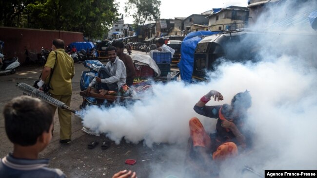 FILE - People react as a civic worker fumigates a slum area as a preventive measure against malaria and dengue ahead of monsoon in Mumbai, India, June 12, 2020.