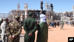 En esta foto del 31 de enero, de 2013, solados argelinos y autoridades frente a una planta de gas en Ain Amenas, vista al fondo, durante una visita organizada por autoridades argelinas para la prensa. EE.UU. dice que lanzó un ataque aéreo el 13 de junio, de 2015, contra el líder de al-Qaeda Mokhtar Bel Mokhtar, al quien responsabiliza por toma de la instalación.