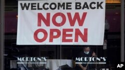 FILE: A sign reading "Welcome Back Now Open" is posted on the window of a Morton's Steakhouse restaurant as a man works inside in San Francisco. Taken Mar. 4, 2021