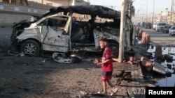 Seorang anak laki-laki berdiri di dekat sebuah mobil yang meledak di Sadr City, dekat Baghdad (28/10).