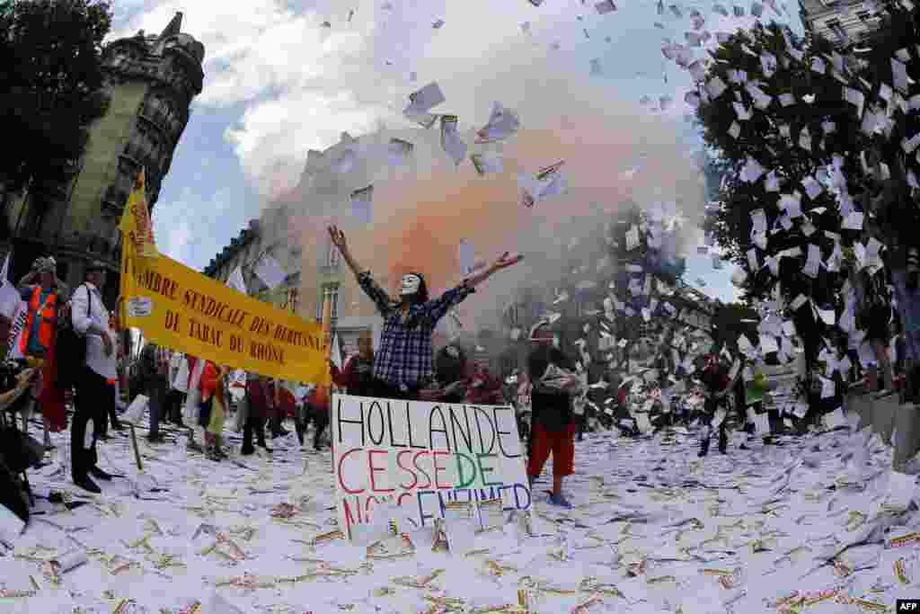 A protester wearing a Guy Fawkes mask stands among a group of protesters from tobacconist groups throwing papers in the air in oppostion to neutral cigarette packaging in Paris, France. Government officials claim the packaging will help reduce the attractiveness of the product, while the tobacco industry claims plain packing will permit easier means of producing counterfeit cigarettes.