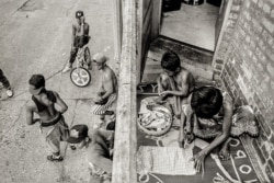 In early 1990s Chicago, in the Uptown neighborhood on the north side, young Cambodian men hang out in a back alley of an apartment building and an elderly Cambodian woman and young boy work with krama, a traditional Khmer textile. (Stuart Isett)