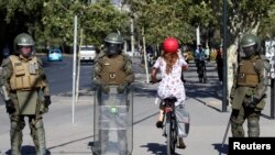 A woman rides a bicycle past police during a protest against Chile's government in Santiago, Chile, Dec. 4, 2019.