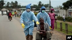 Les habitants du quartier Saint-Paul Pont couverts d’un équipement de protection individuelle transportent un homme soupçonné de porter le virus Ebola à la Clinique île à Monrovia, au Libéria, le dimanche 28 septembre 2014.Six months into the world’s worst-ever Ebola outbreak, a