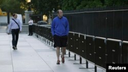 FILE - Pedestrians walk by a lower, portable fence that was placed in front of the White House in Washington to establish a security buffer zone after an intruder, Omar Gonzalez, cleared the taller fence last year.