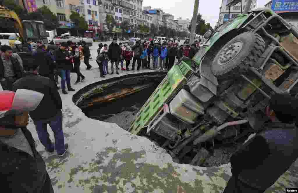 People look at a loaded truck that got stuck in a sinkhole on a road in Guilin, Guangxi Zhuang Autonomous Region, China.
