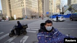 Mensajeros hacen su trabajo con máscaras protectoras en un desolado distrito comercial de Beijing, China, el 18 de febrero de 2020.