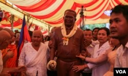 រូបឯកសារ៖ ម្ដាយលោកកែម ឡី (ខាងឆ្វេងរូបសំណាក់លោកកែម ឡី) និងបងស្រីលោកកែម ឡី(ខាងស្ដាំ) រំកិលរូបសំណាកស្ពាន់តំណាងលោកកែម ឡីអ្នកវិភាគកិច្ចអភិវឌ្ឍន៍សង្គមដែលត្រូវខ្មាន់កាំភ្លើងបាញ់ស្លាប់ នៅស្រុកកំណើតលោកនៅខេត្តតាកែវ នៅថ្ងៃអាទិត្យ ទី១៧ ខែតុលា ឆ្នាំ២០១៦។ (ឡេង ឡែន/វីអូអេ)