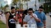 چند مرد جوان در حال خواندن تابلوی ضوابط ایمنی کووید ۱۹ هستند - میامی، فلوریدا - ۲۷ مارس ۲۰۲۱