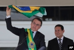 Brazil's President Jair Bolsonaro, flanked by his Vice President Hamilton Mourao, waves the national flag from the Planalto Presidential palace, in Brasilia, Brazil, Jan. 1, 2019.