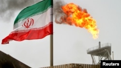 FILE - A gas flare on an oil production platform in the Soroush oil fields is seen alongside an Iranian flag in the Persian Gulf, Iran, July 25, 2005.