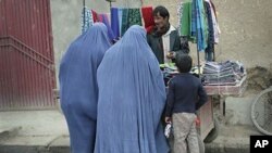 Afghan women clad with burqas buy scarves from a street vendor man in Kabul, Afghanistan, Nov. 23, 2011. A law meant to protect Afghan women from a host of abusive practices, including rape and forced marriage, is being undermined by spotty enforcement, t