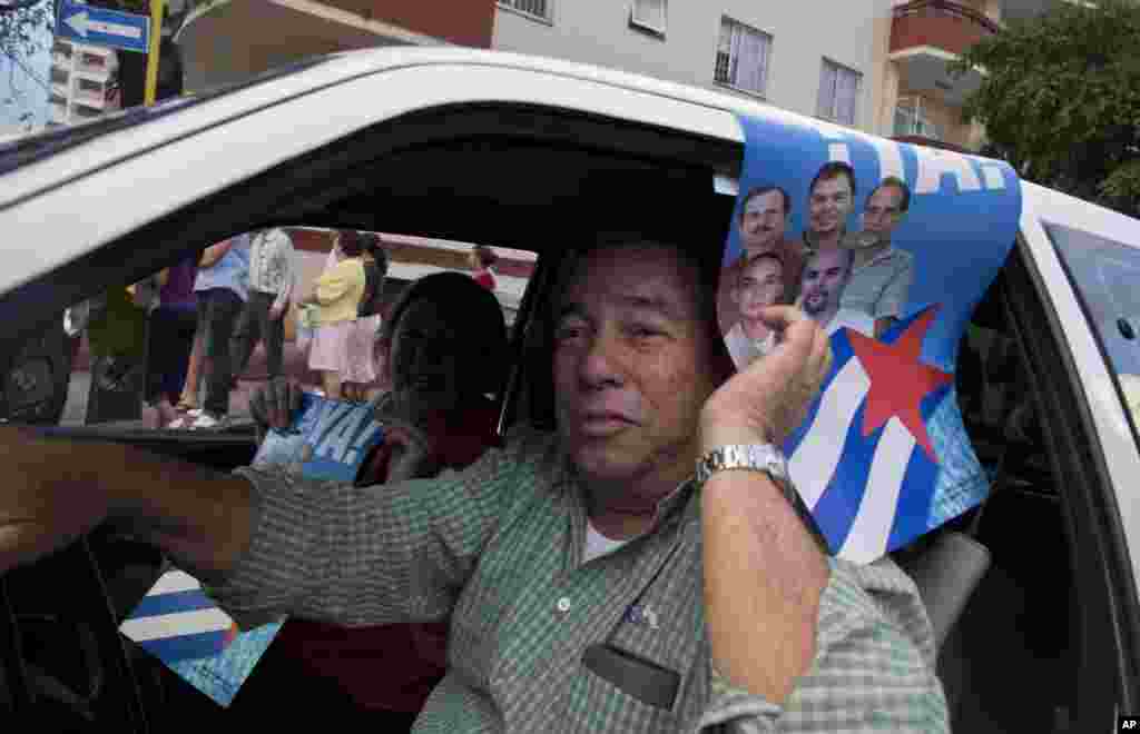Seorang pria mengendarai mobil sambil memegang poster bergambarkan the Cuban Five -- lima orang pejabat intelijen Kuba yang ditangkap oleh AS -- untuk merayakan kebebasan mereka di Havana, Kuba (17/12). (AP/Ramon Espinosa)