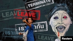 A woman takes a "selfie" in front of a banner with a caricature of the caretaker Prime Minister Yingluck Shinawatra displayed inside an anti-government protest encampment in central Bangkok, Feb. 25, 2014.