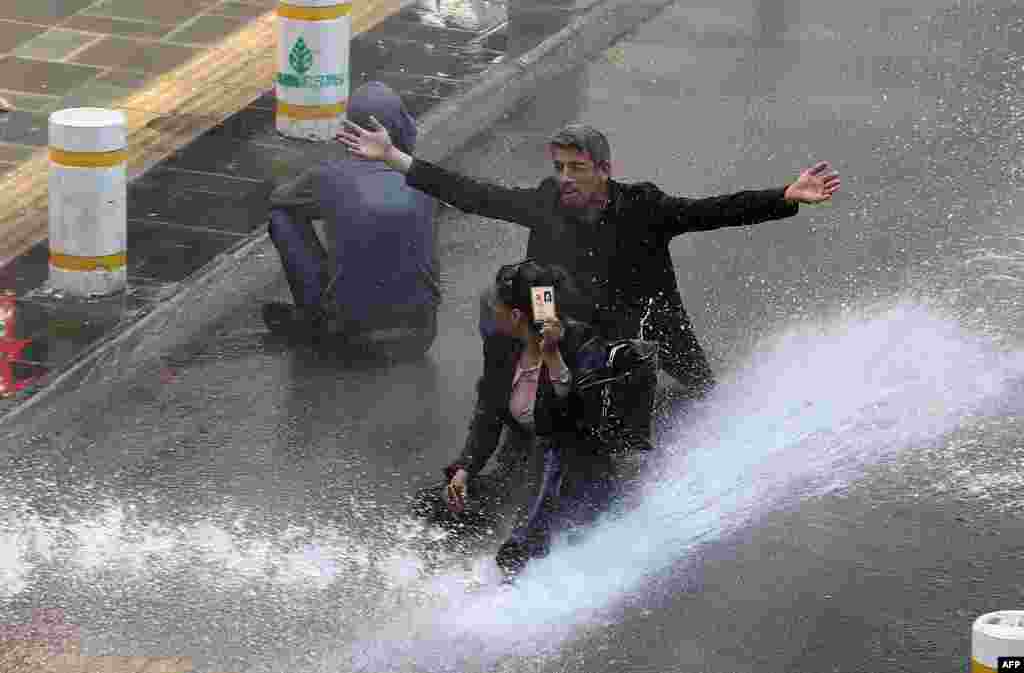 A woman shows her identity card as riot police use water cannons during clashes on May Day in Ankara, Turkey.