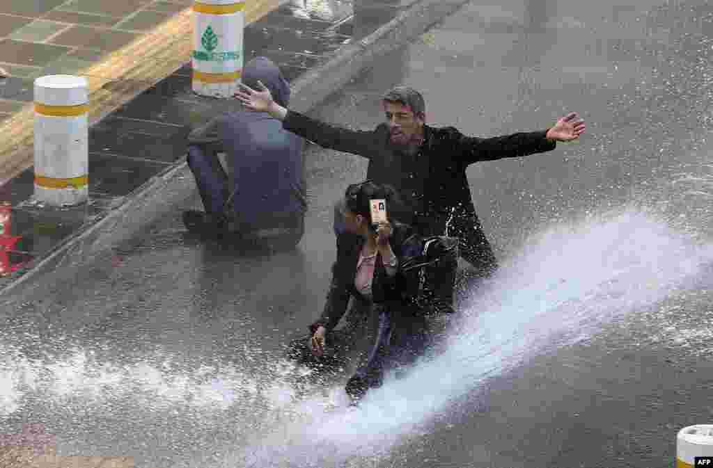 A woman shows her identity card next to another protester as riot police use water cannons during clashes after hundreds of people tried to reach the city&#39;s main Kizilay Square to celebrate May Day in Ankara, Turkey.