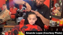 Austin Lopez reads a book to Amir Shalash as he gets his hair cut at Prince Cuts Barbershop, Lexington, KY