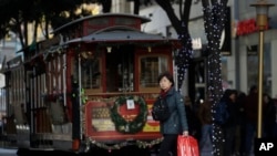 Una mujer lleva una bolsa de compras mientras camina frente a un tranvía en San Francisco, el viernes 29 de noviembre de 2019. (Foto AP/Jeff Chiu).