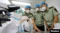 FILE - A health inspection and quarantine researcher, left, demonstrates to customs policemen the symptoms of Ebola, at a laboratory at an airport in Qingdao, Shandong province, Aug. 11, 2014. 