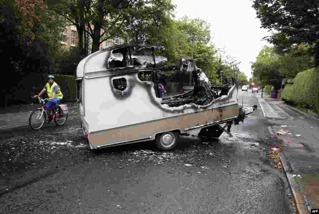 August 10: A cyclist passes the burnt shell of a camper after overnight rioting and looting in the neighbourhood of Toxteth in Liverpool, northern England. British cities began on Wednesday to clean up shopping streets littered with debris from looting by