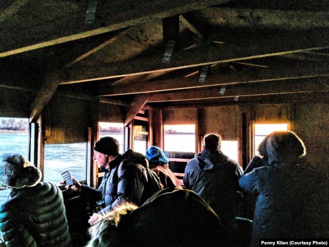 As the sun rises, crane watchers look out the holes in the blinds at Aububon's Rowe Sanctuary to spot sandhill cranes perched on the river or flying overhead, near Gibbon, Neb., March 16, 2019.