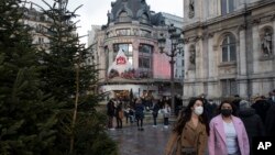 Women wearing face masks to prevent the spread of the COVID-19, walks past City Hall, in Paris, Dec. 26, 2021.