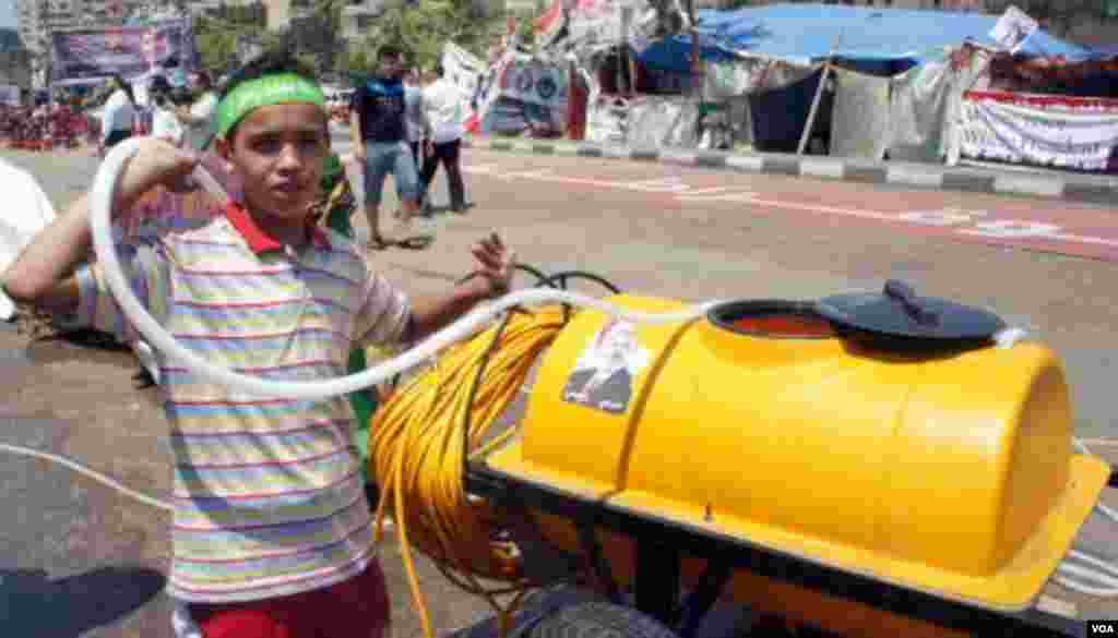 Seorang anak laki-laki bersiap menyiram air ke kerumunan di tengah teriknya matahari Kairo (12/8). (VOA/E. Arrott) 