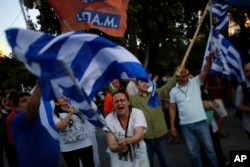 A supporter of the No vote waves a Greek flag after the referendum's exit polls at Syntagma square in Athens, Sunday, July 5, 2015.