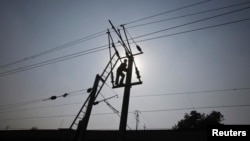 A technician is silhouetted as he works on power lines supplying electricity in the outskirts of Lahore, Pakistan, Jan. 31, 2012.