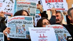 FILE - Demonstrators hold placards and copies of the Cumhuriyet daily newspaper at a protest outside an Istanbul court where about a dozen employees of the newspaper are being tried on charges of aiding terror groups, Oct. 31, 2017.