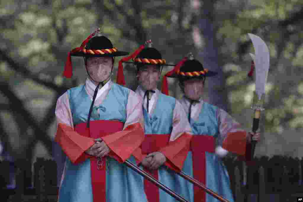 Performers wearing traditional guard clothes and protective face masks stand during a re-enactment ceremony of the changing of the Royal Guards, in front of the main gate of the Deoksu Palace in Seoul, South Korea.