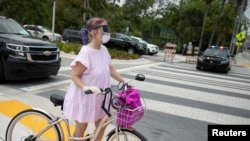 Una mujer utiliza una máscara protectora mientras pasea con su bicicleta por Miami Beach, Florida, el 8 de abril de 2020.