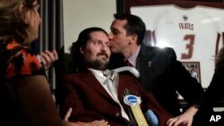 FILE - Former Boston College baseball captain Pete Frates, seen center left in this Dec. 13, 2016 photo, receives a kiss from Boston College head baseball coach Mike Gambino after Frates was presented with the 2017 NCAA Inspiration Award, during ceremonies in Frates home in Beverly, Mass.