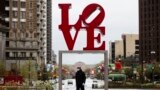 A person wearing a protective face mask and gloves as a precaution against the coronavirus walks by the Robert Indiana sculpture "LOVE" at John F. Kennedy Plaza, commonly known as Love Park, in Philadelphia, Monday, April 13, 2020. (AP Photo/Matt Rourke)