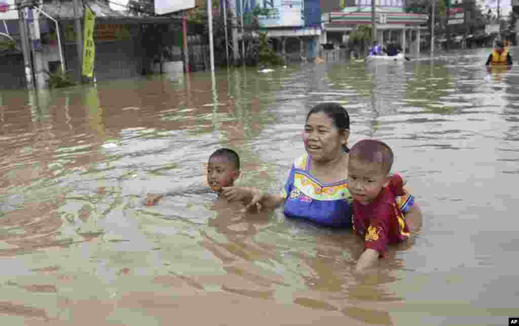 Seorang ibu membawa dua anaknya mengarungi banjir di Jakarta (13/1). (AP/Achmad Ibrahim)