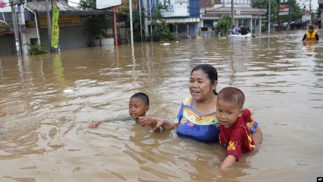 Seorang ibu membawa dua anaknya mengarungi banjir di Jakarta (13/1). (AP/Achmad Ibrahim)