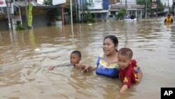 Seorang ibu membawa dua anaknya mengarungi banjir di Jakarta (13/1). (AP/Achmad Ibrahim)