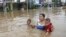 Seorang ibu membawa dua anaknya mengarungi banjir di Jakarta (13/1). (AP/Achmad Ibrahim)