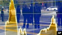 In this April 8, 2016 file photo, people are reflected on the electronic board of a securities firm in Tokyo. The IMF downgraded its outlook for growth for most regions and for the global economy as a whole. 