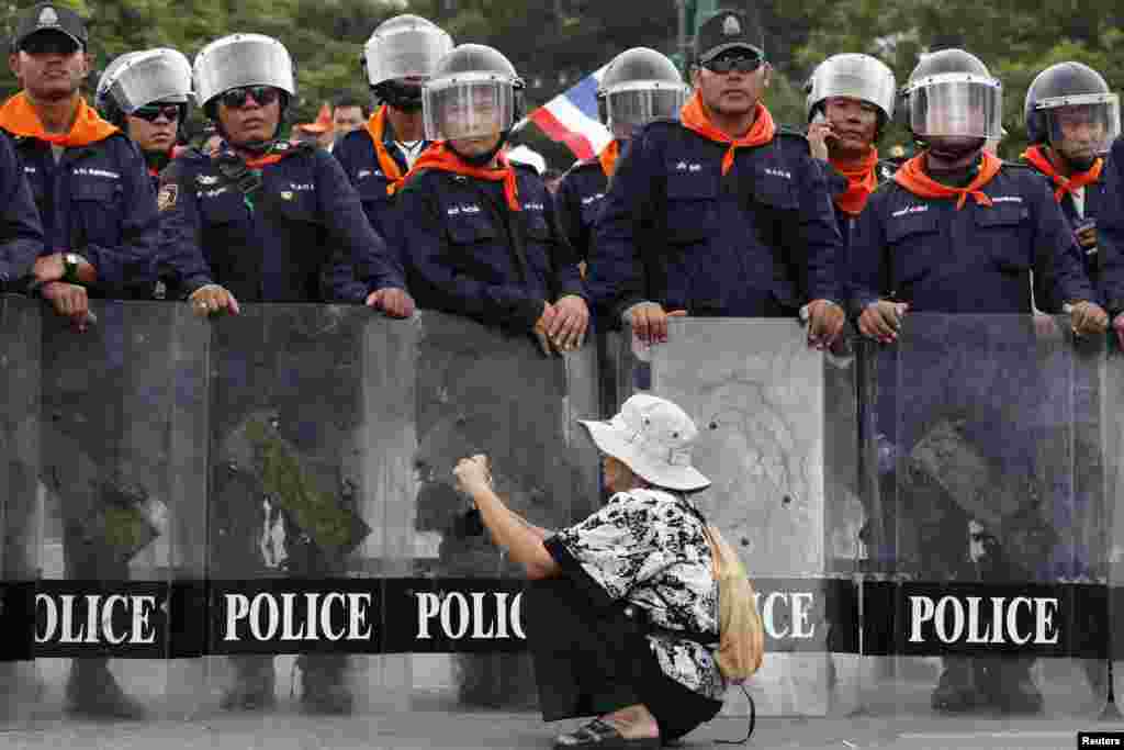 A woman takes pictures in front of a line of policemen blocking protesters against an amnesty bill, on the main road near the government and parliament buildings in central Bangkok, Thailand. The Thai Senate will likely reject an amnesty bill which critics say is aimed at bringing back convicted former premier Thaksin Shinawatra from exile, the Senate Speaker said.