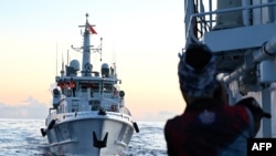 FILE - A Philippines coast guard member looks at the Chinese Coast Guard vessel as they come close during a mission to deliver provisions at Second Thomas Shoal in the South China Sea on November 10, 2023.